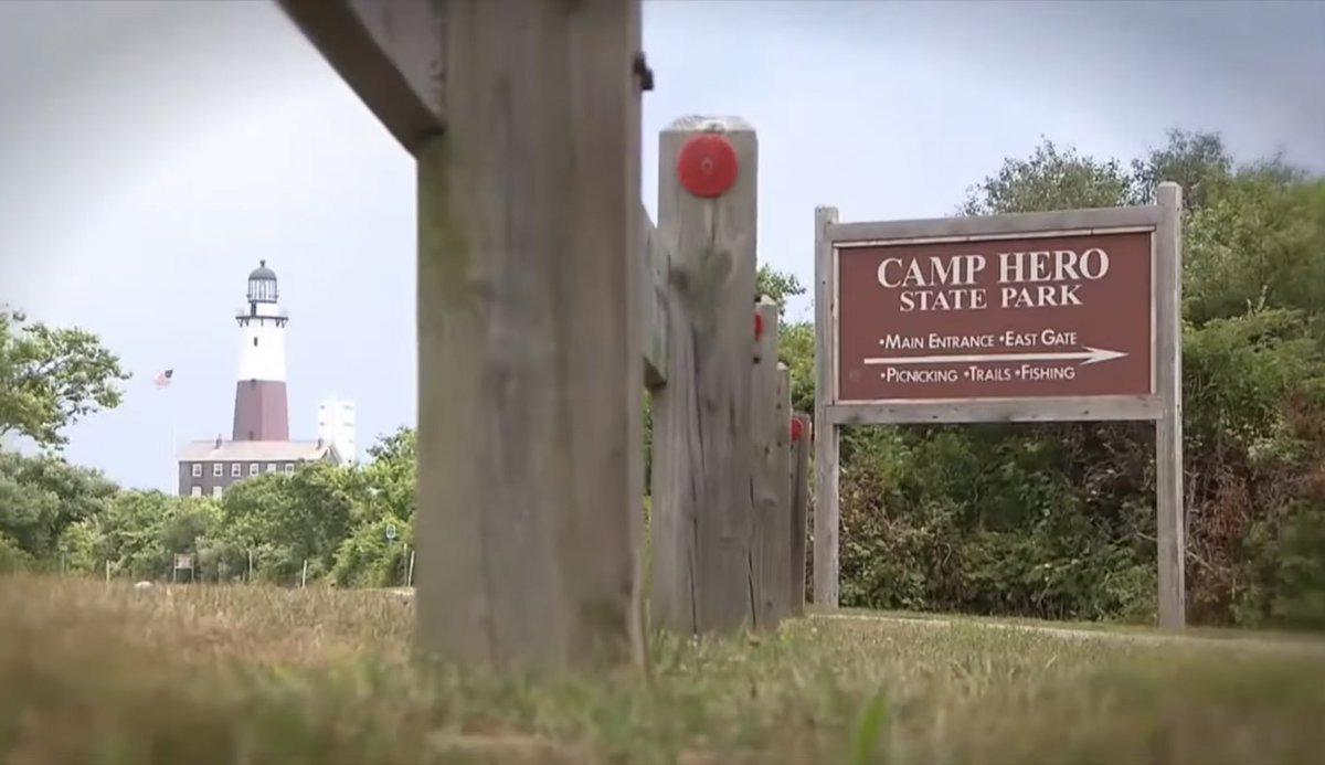 The Montauk lighthouse visible past a wooden Camp Hero State Park trail sign.